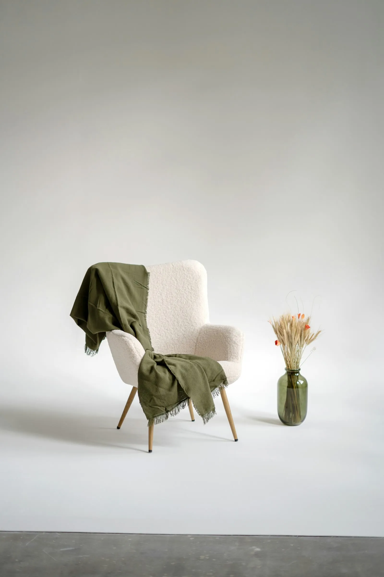 A gray armchair with a green wool throw beside a vase of dried grasses