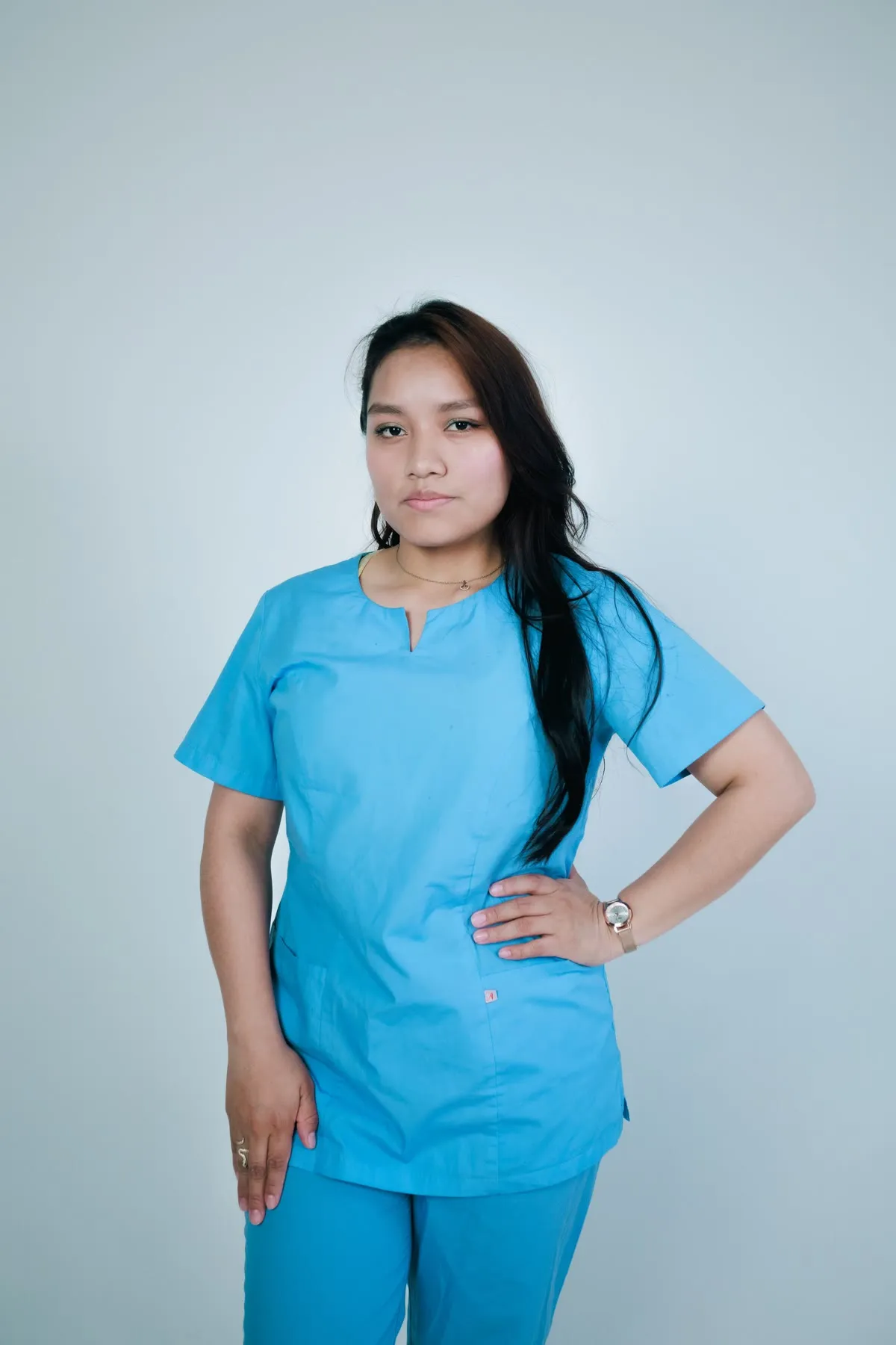 A nurse in light blue scrubs, standing with one hand on her hip
