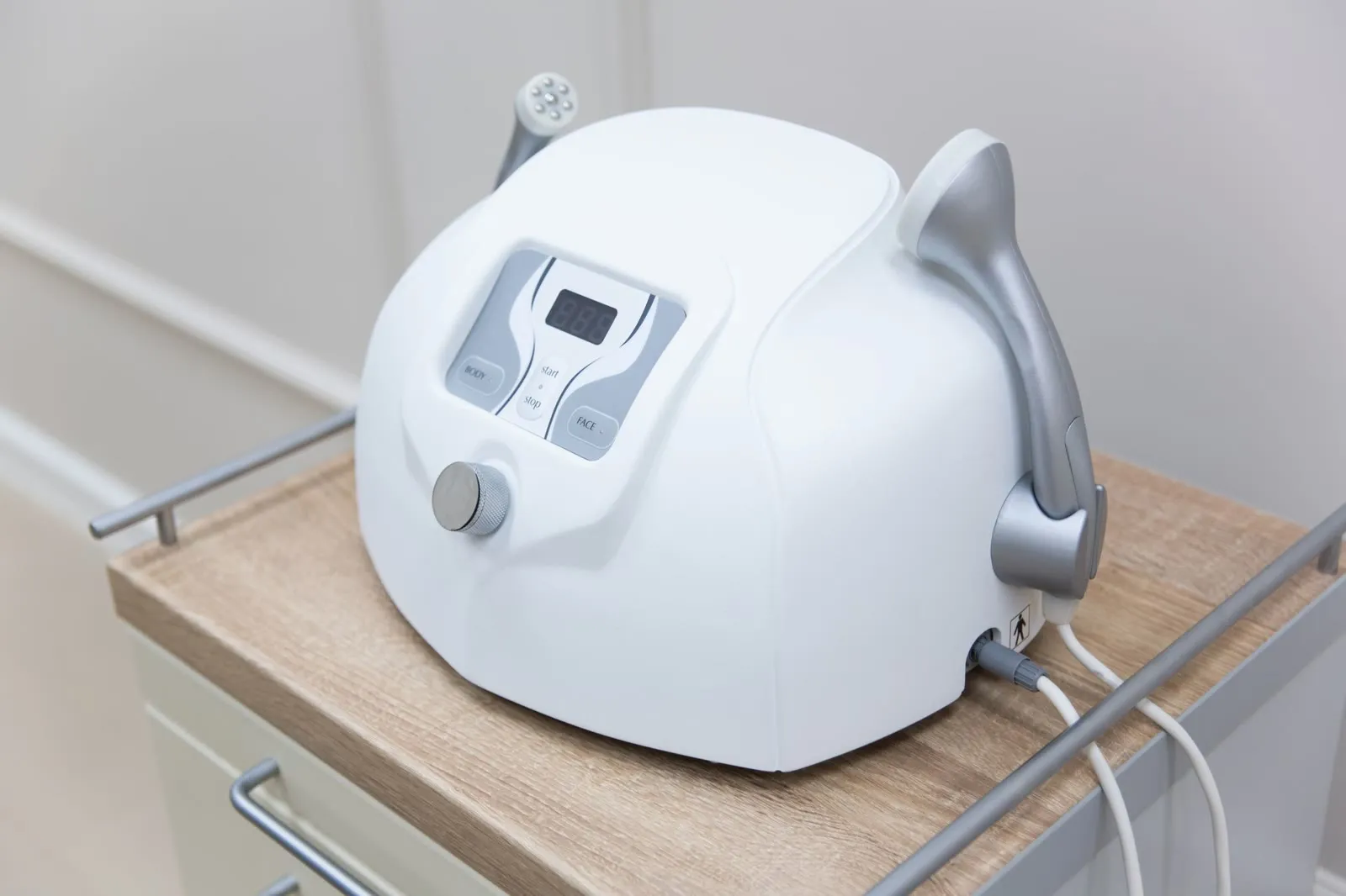 A white skin treatment device with two handpieces on a wooden cart